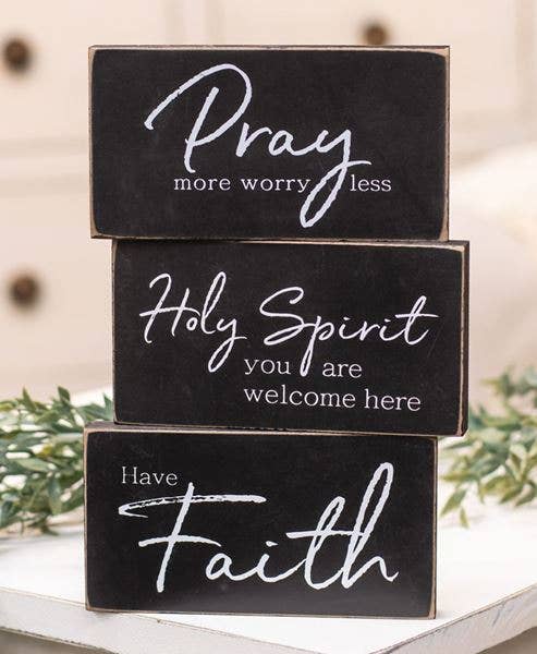 Black wooden block signs with white lettering reading “Pray more worry less,” “Holy Spirit you are welcome here,” and “Have Faith.”