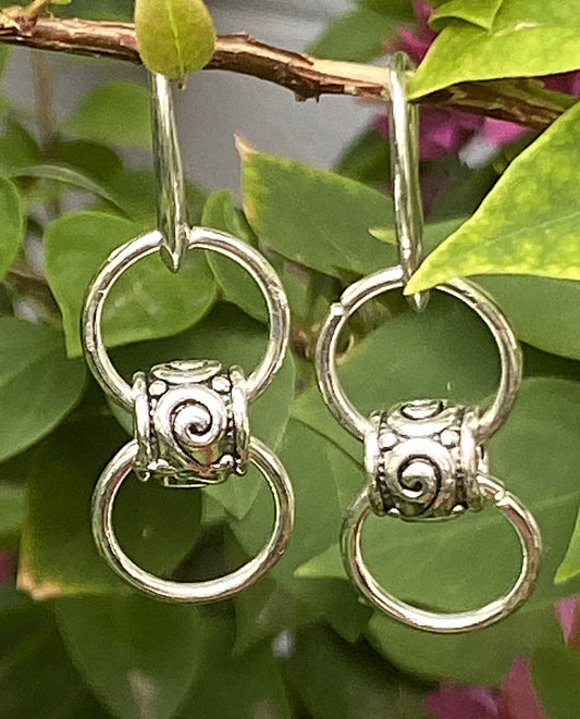 Silver-toned earrings with three interlocking rings, swirl detail on center ring, ear wire style with silicone nugs, approx. 1¾ inches long.