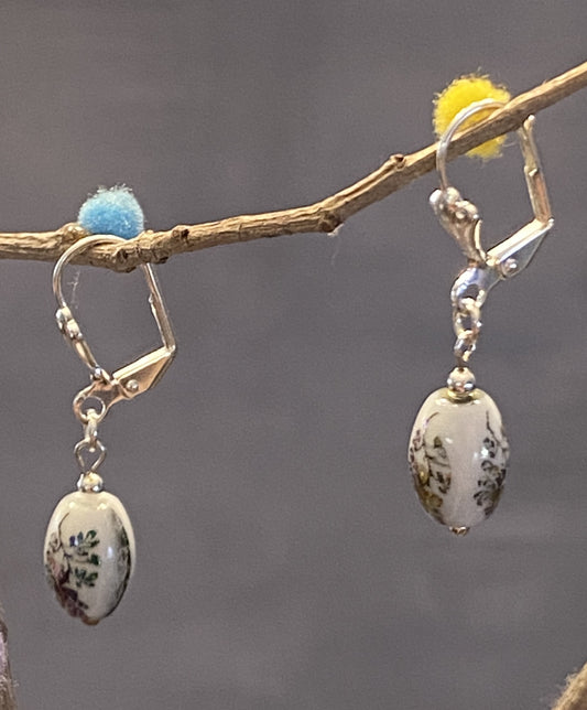 Hazel earrings feature white glass beads with a delicate flower design. Silver-toned base metal, lever backs, approx. 1½" long. Elegant and timeless charm.