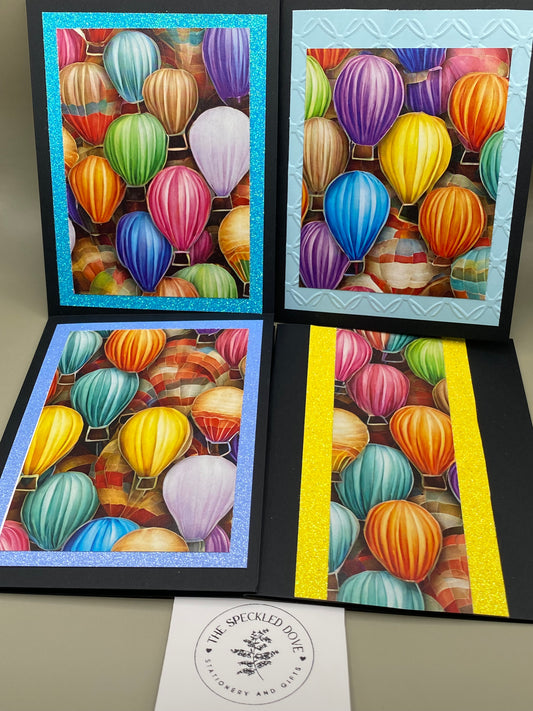 Set of 4 hot air balloon note cards with black base and glitter cardstock layers. Blank inside. Each card measures 4 1/4" x 5 1/2". Includes envelopes.
