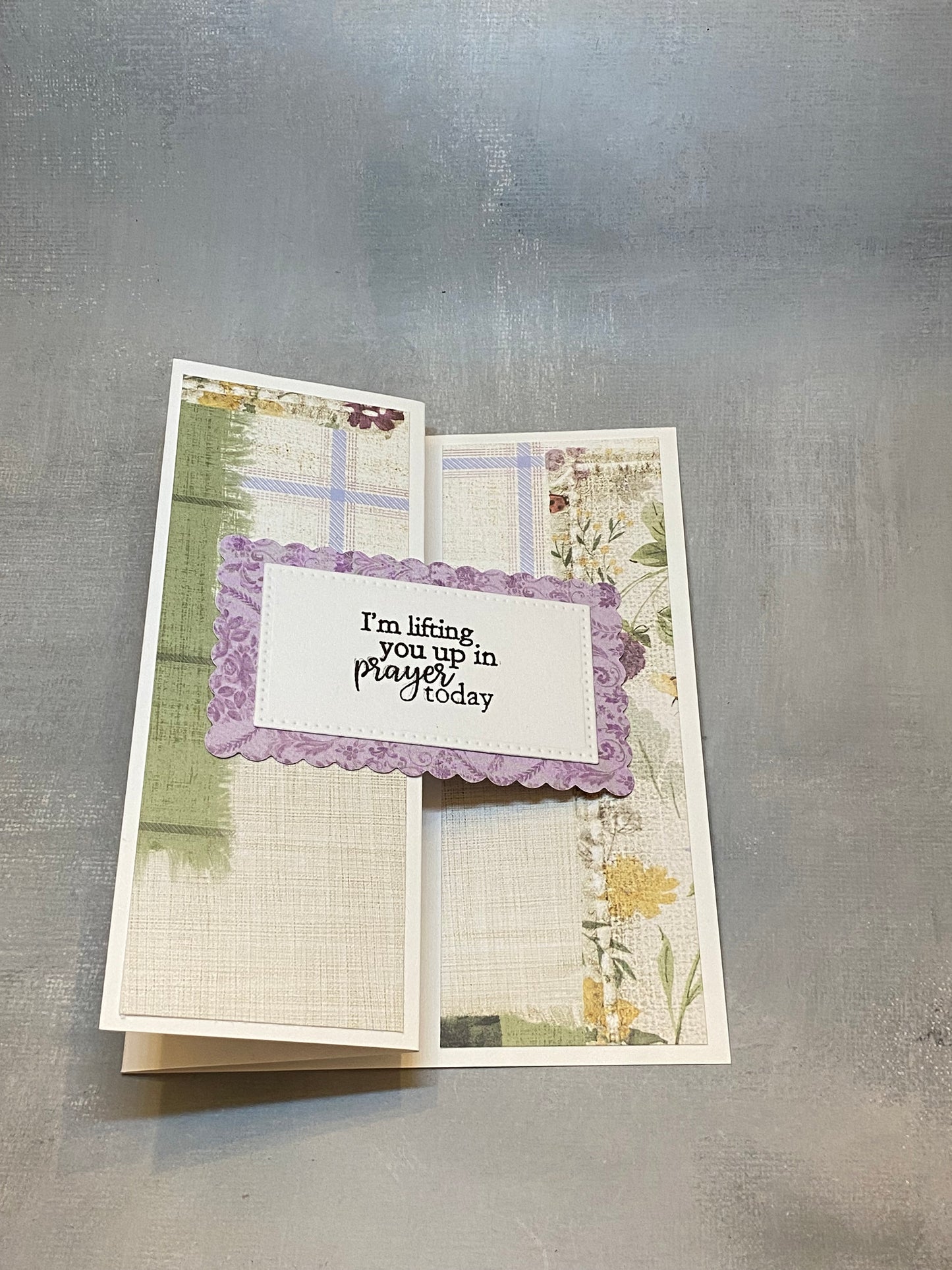 "Sympathy card with a green and purple floral background, hand-stamped with 'I'm lifting you up in prayer today,' shown with a white envelope."