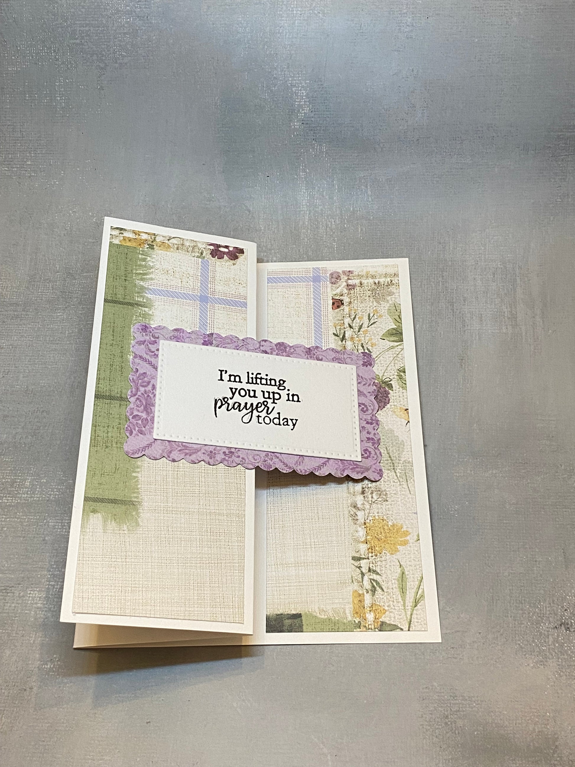 "Sympathy card with a green and purple floral background, hand-stamped with 'I'm lifting you up in prayer today,' shown with a white envelope."