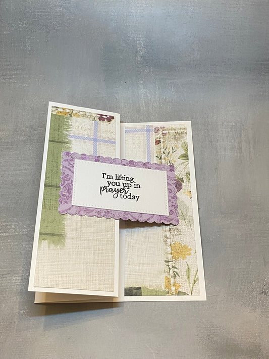 "Sympathy card with a green and purple floral background, hand-stamped with 'I'm lifting you up in prayer today,' shown with a white envelope."